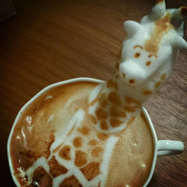 3D latte art of a giraffe with a long neck rising from a coffee cup.