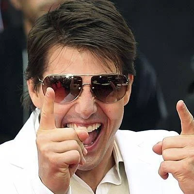 Laughing Tom Cruise — Tom Cruise with extreme grin expression wearing sunglasses and giving a thumbs-up gesture in a clean photograph.