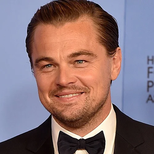 Leonardo DiCaprio in a black tuxedo and bow tie smiling at a press event