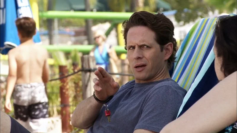 Lie Back Down — A clean single-shot capturing the man's distinctive facial expression and hand gesture in the park setting, representing the core reaction