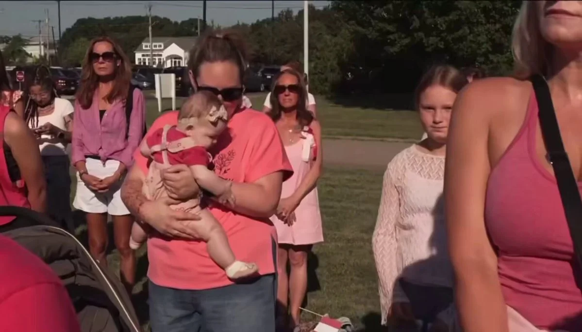 Lindsay Clancy Trial — Group of women and children wearing pink shirts and dresses gathered outdoors, one holding a baby in a pink outfit.