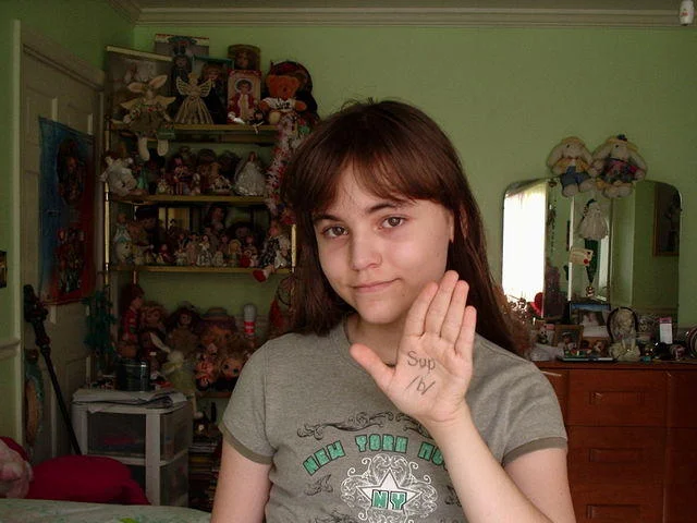 Loli-chan — Girl in bedroom holding up hand with 'Sup /b/' written on her palm