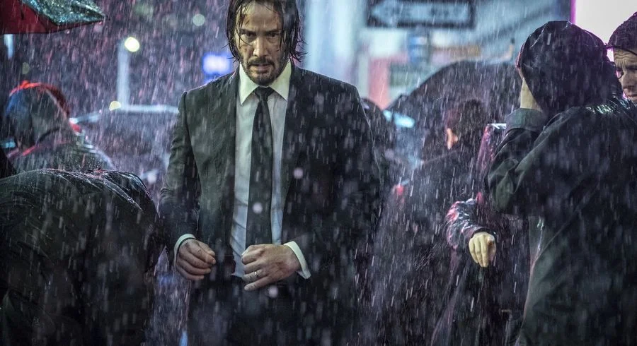 Lonely Keanu — Keanu Reeves as John Wick standing alone in the rain wearing a black suit
