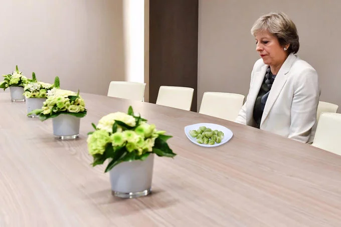 Lonely Theresa May — Theresa May alone at conference table with a plate of Brussels sprouts photoshopped in front of her.