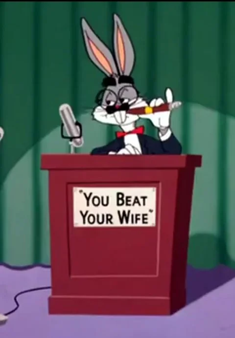Looney Tunes — Bugs Bunny in a tuxedo and fake mustache at a courtroom podium with a sign reading 'You Beat Your Wife'.