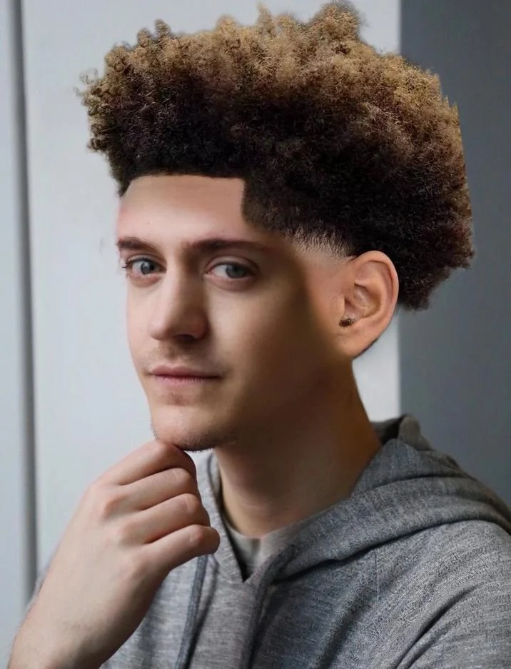 A high-quality professional portrait of a person displaying a textbook low taper fade with voluminous textured hair on top and sharply faded sides.