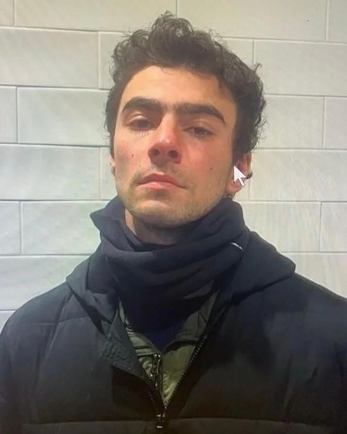Luigi Mangione Is Not The Shooter Conspiracy Theory — Luigi Mangione in black jacket and neck gaiter after arrest