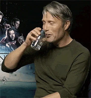 Mads Mikkelsen Opening Vodka During Interview — A crisp photograph of actor Mads Mikkelsen holding a glass to his lips during interview with Rogue One poster