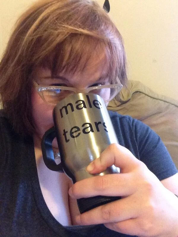 Woman in glasses drinking from a silver Male Tears mug