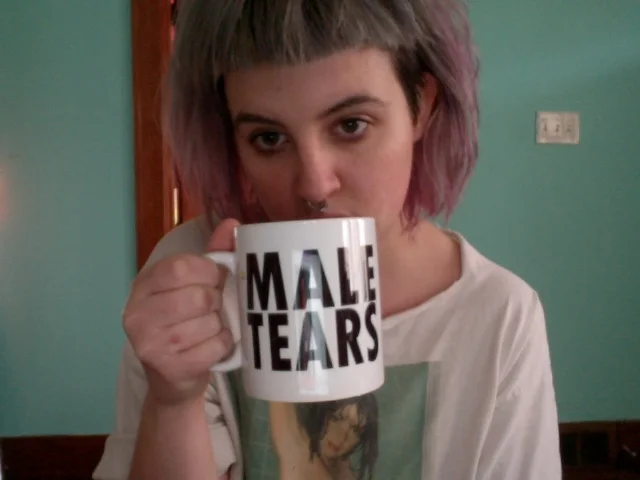Person with purple hair drinking from a Male Tears mug