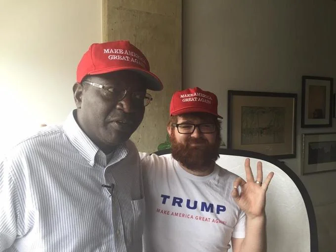 Malik Obama posing with a bearded Trump supporter both wearing MAGA hats
