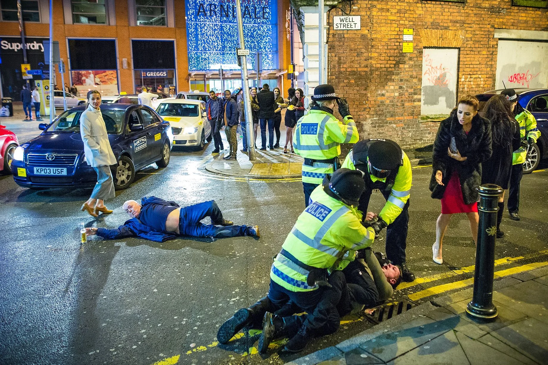 Manchester New Year's Eve Photo — Man lying on Manchester street holding a beer bottle as police restrain another man on Well Street
