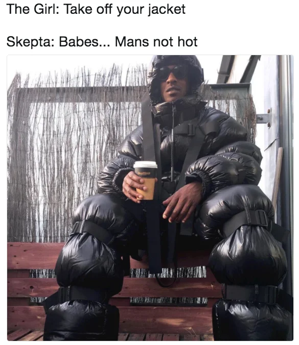 Skepta sitting on steps in oversized puffer suit with 'Mans not hot' caption