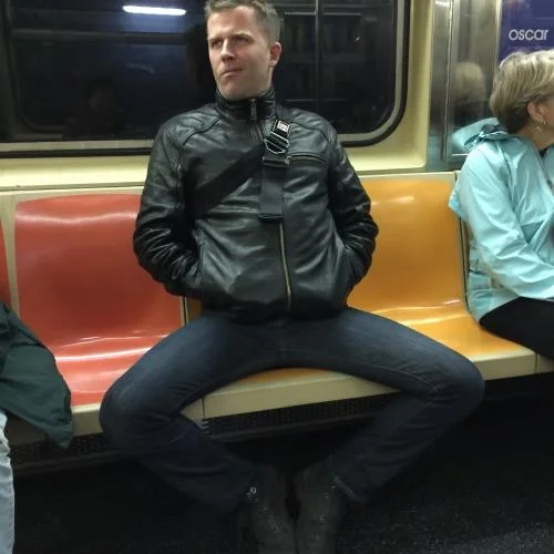 Man in leather jacket manspreading on subway bench