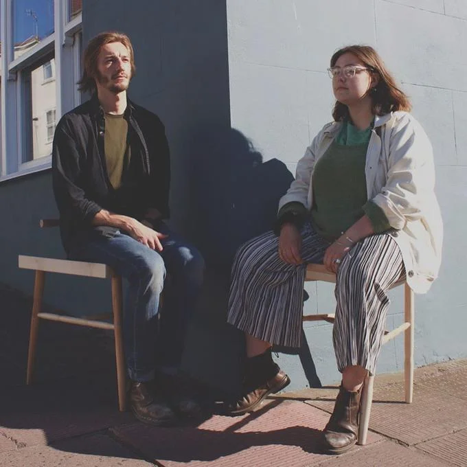 Woman and man sitting on differently sized stools demonstrating anti-manspreading design