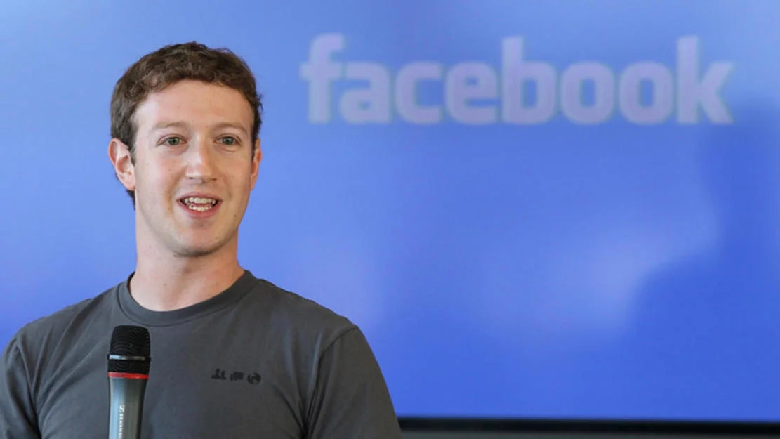 Mark Zuckerberg smiling with microphone in front of Facebook logo