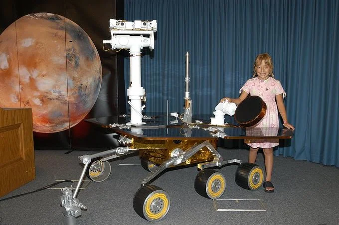 Mars Exploration — Child posing beside a full-scale Mars rover model at a NASA display