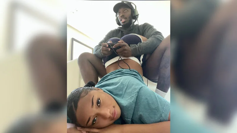 Megan Thee Stallions Butt In Gamer Boyfriends Face — A person lies face-down on the floor with arched back positioned below a gaming boyfriend wearing