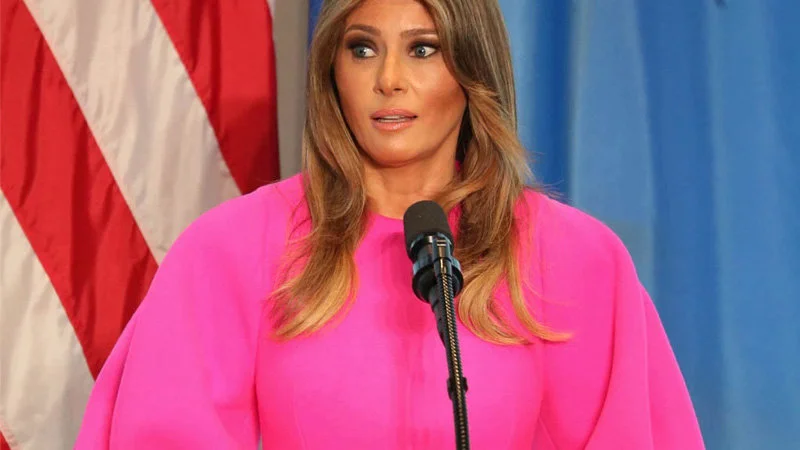 Melania Trumps Un Speech Dress — Clean, high-resolution press photograph of Melania Trump standing at a microphone at the United Nations in her bright fuchsia