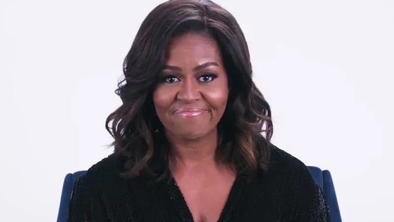 Michelle Obamas Hey Queen — Michelle Obama smiles warmly at the camera with an encouraging, approving expression in a dark blue and black outfit.