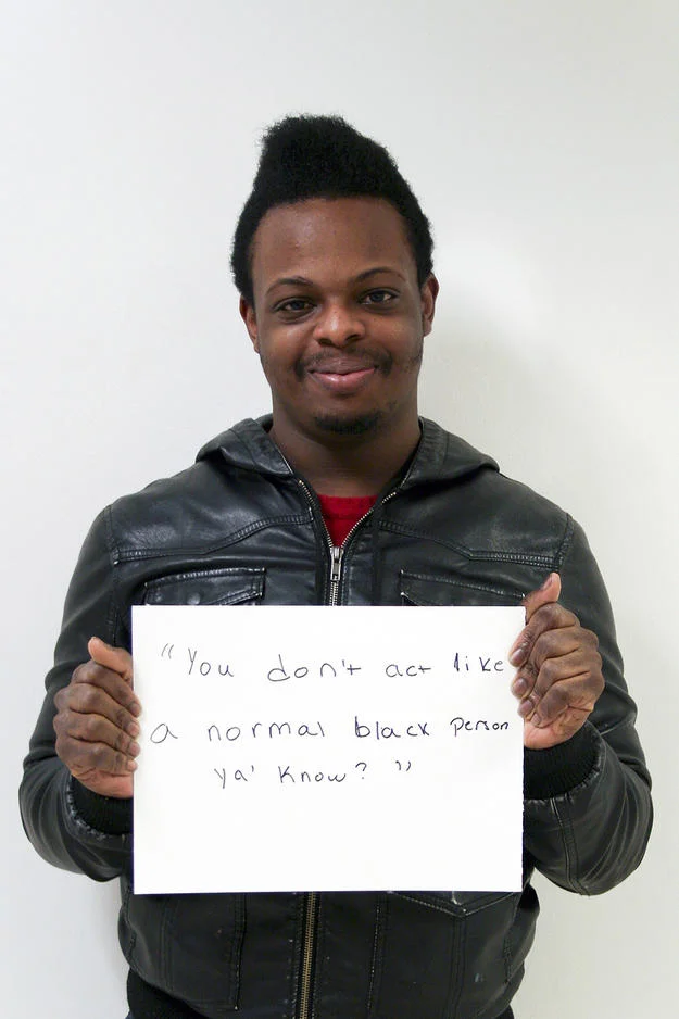 Microaggression — Black man in leather jacket holding sign reading 'You don't act like a normal black person ya know?'