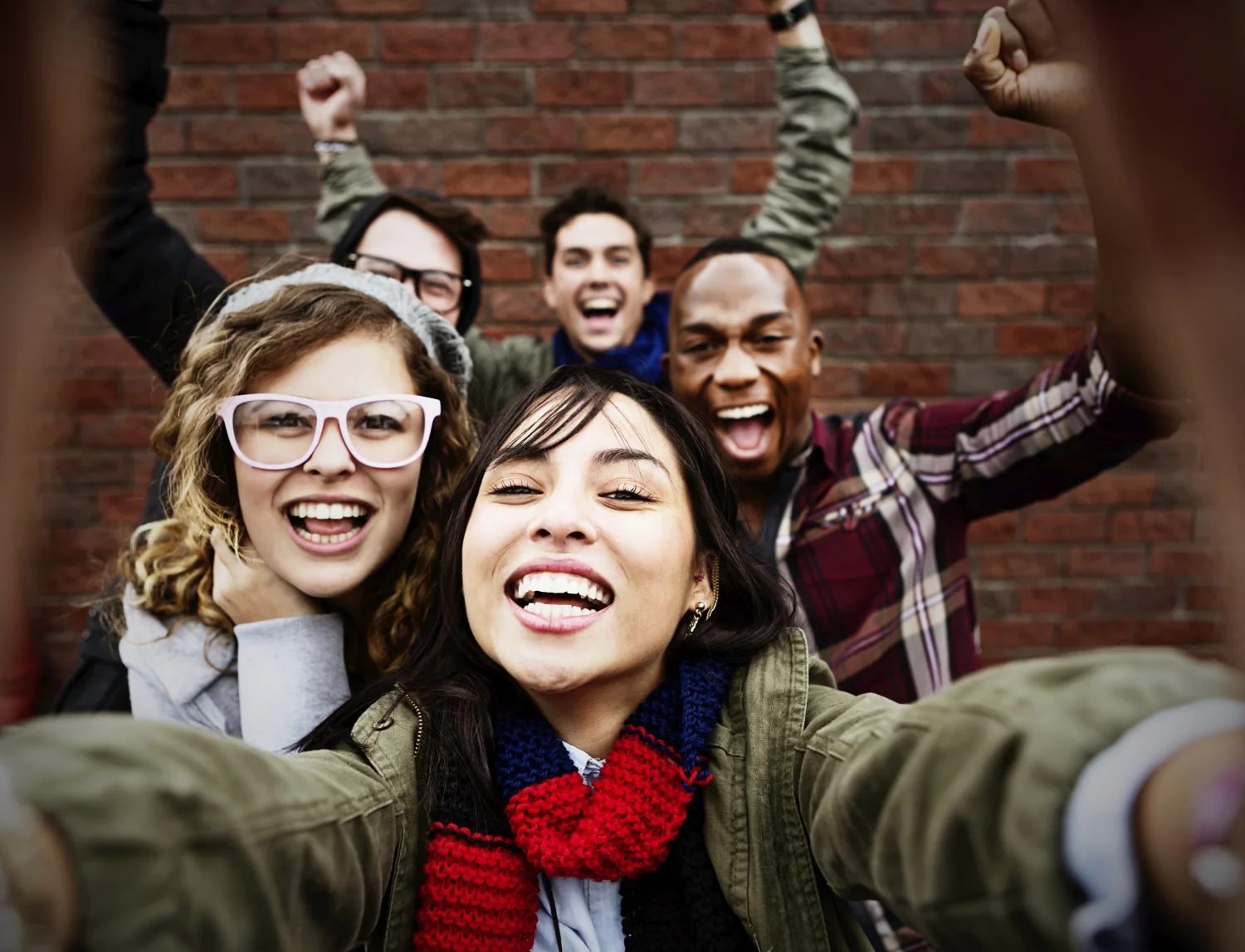 Group of cheering young millennials taking a selfie in front of a brick wall