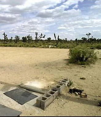 Mojave Phone Booth — Desert landscape with Joshua trees showing scattered concrete blocks and foundation where booth stood.