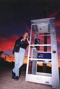 Mojave Phone Booth — Person leaning against open phone booth speaking into handset silhouetted against desert sunset.