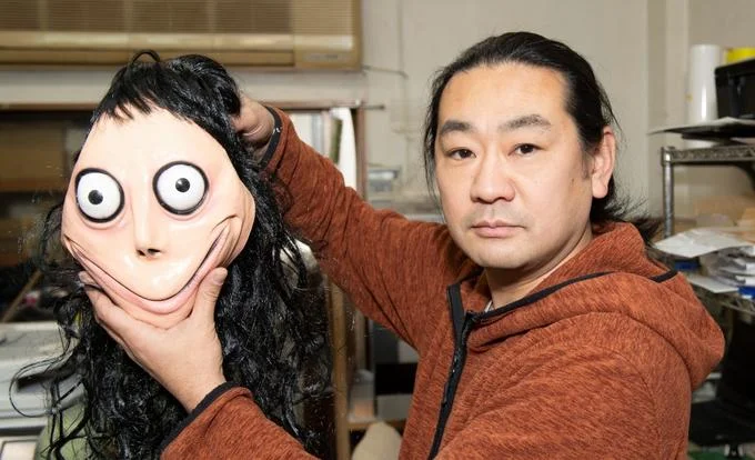 Person holding Momo head mask or prop in front of face posing indoors.