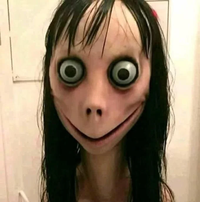 Frontal close-up of Momo sculpture showing large bulging eyes, black hair, and slight smile.