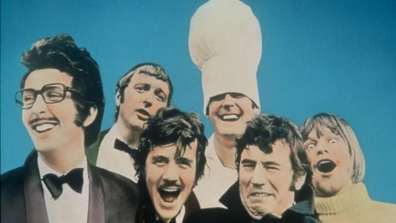 Monty Python troupe group photo with members posing in front of blue sky