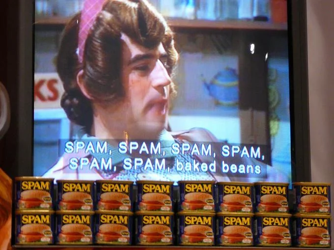 TV showing Monty Python Spam sketch above stack of Spam cans