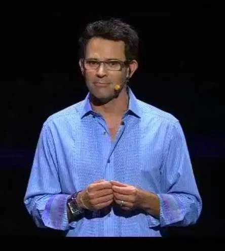 Man in blue shirt and glasses with headset microphone on dark stage, known as Mr. Caffeine