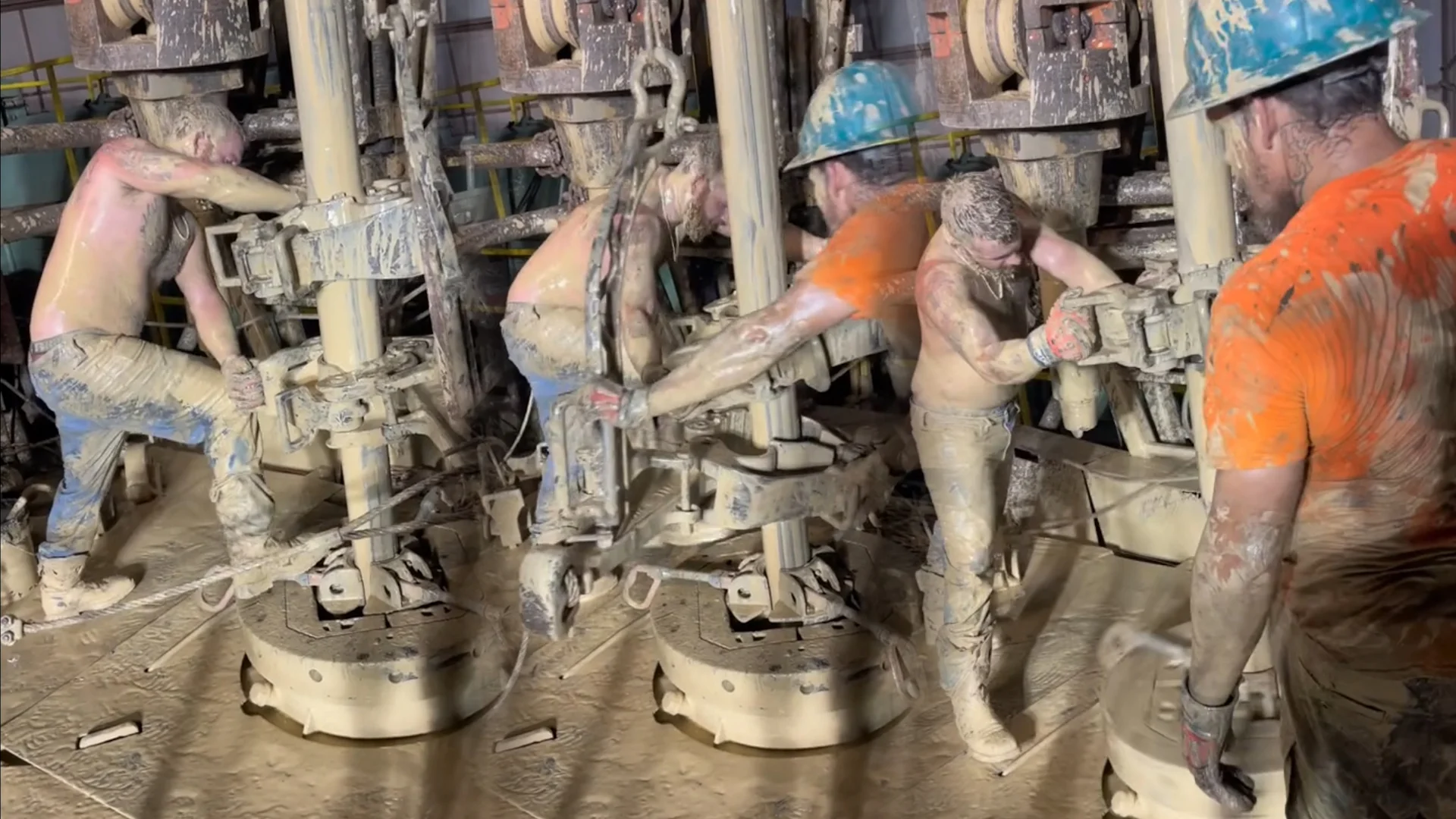 Muddy Workers Operating Machinery — Composite image of several mud-covered shirtless workers in blue hard hats operating heavy drilling machinery on an oil rig.