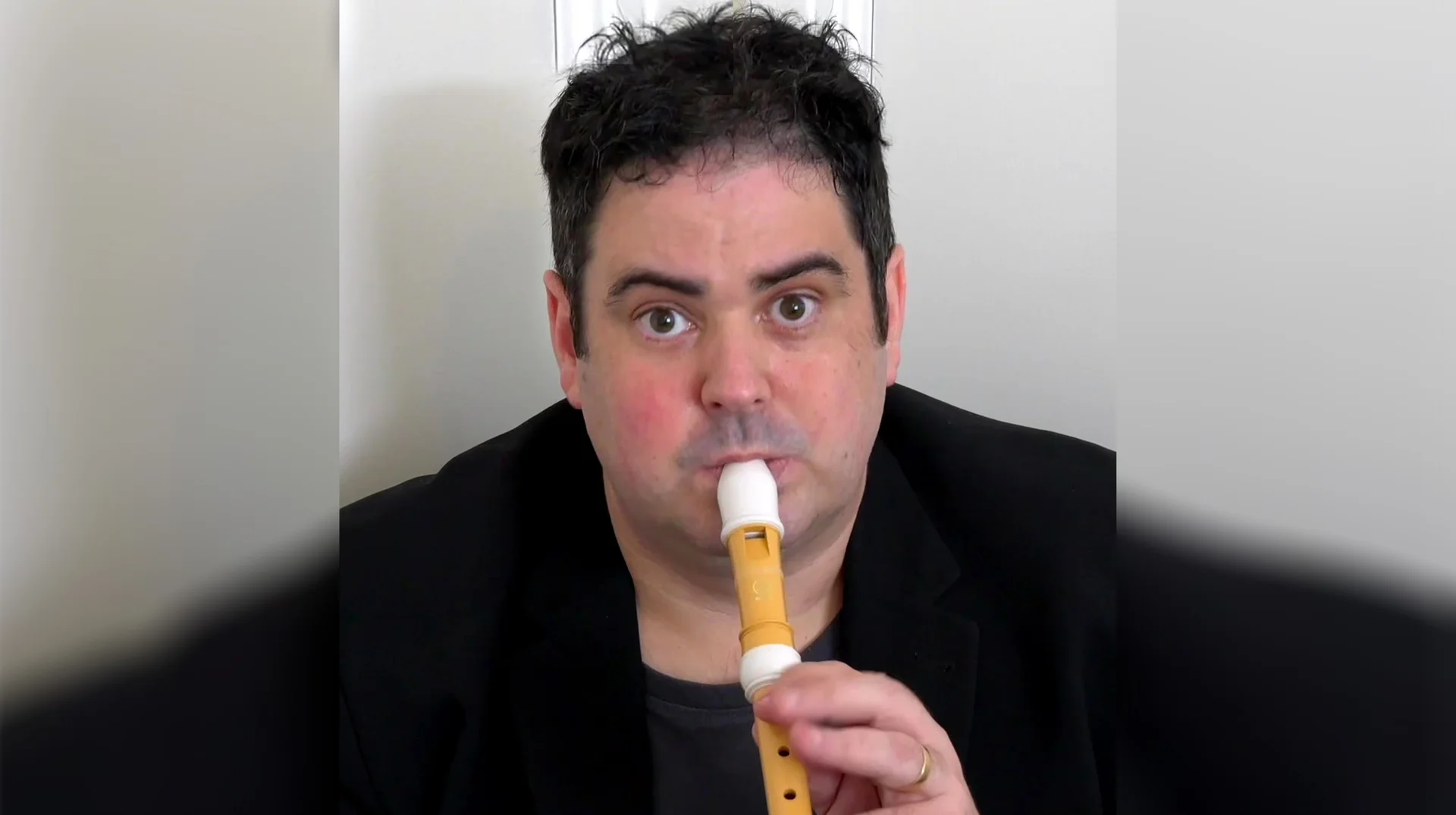 My Name Is Richard and I'm Sitting In the Corner — Man in black blazer playing a recorder flute while staring at camera