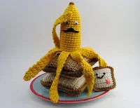 A yellow crocheted or knitted interpretation of Nannerpuss with googly eyes positioned on pancakes.