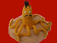 Nannerpuss mascot posed against a vibrant red background, showing the yellow banana body with googly eyes and mustache.
