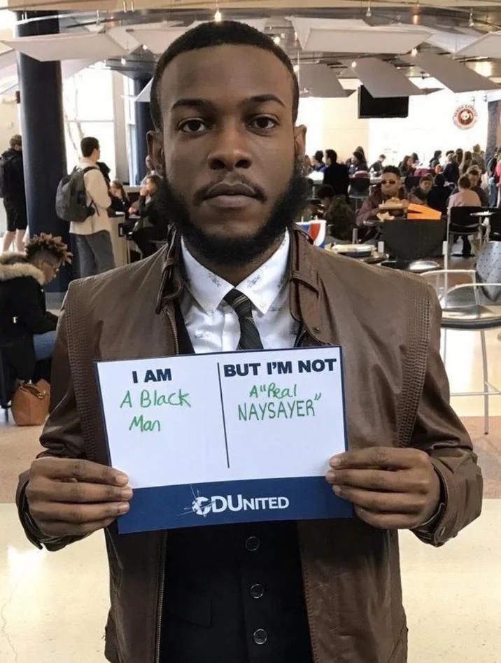 Man holding sign reading 'I am a Black man but I'm not a real Naysayer.'