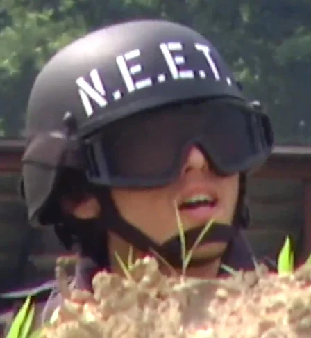 NEET — Person wearing a black tactical helmet stenciled with 'N.E.E.T.' in white