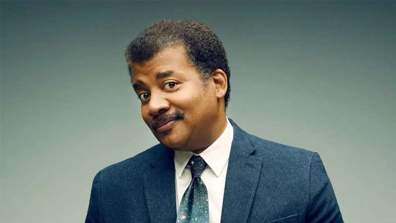 Neil deGrasse Tyson smirking in a dark suit and galaxy tie