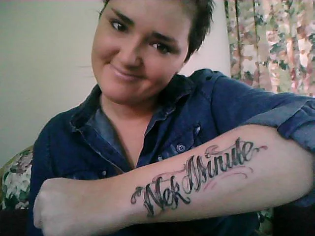 Nek Minnit — Woman displaying a Nek Minute cursive forearm tattoo