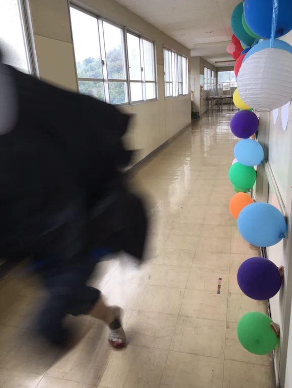 No Face Chasing Chihiro — Close-up of person in black No-Face costume running past colorful balloons