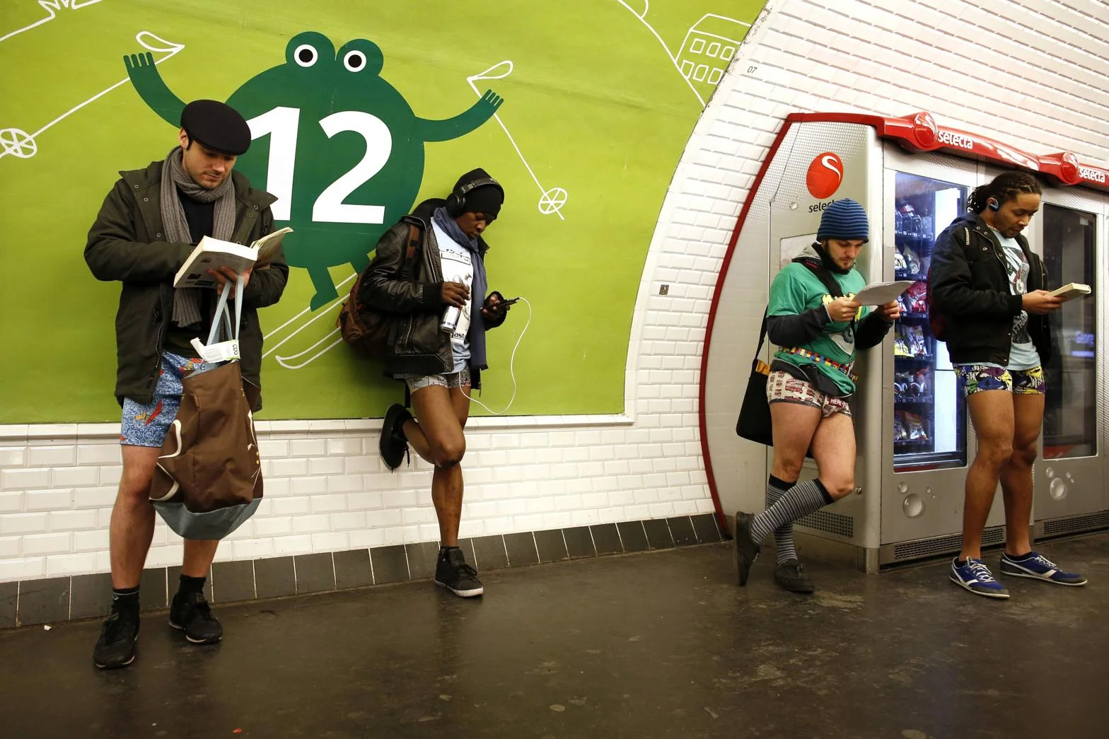 No Pants Subway Ride — Four people without pants on a Paris Metro station platform reading books and checking phones
