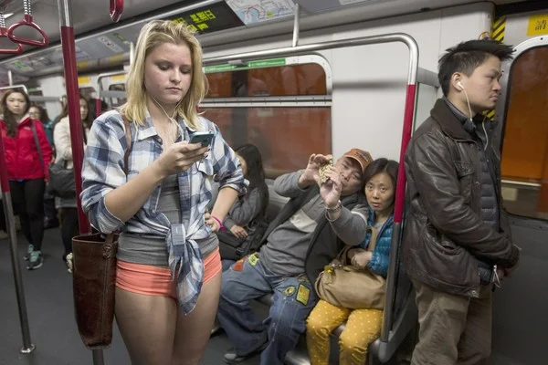 No Pants Subway Ride — Young woman in shirt and shorts standing on a subway train with other pantsless riders