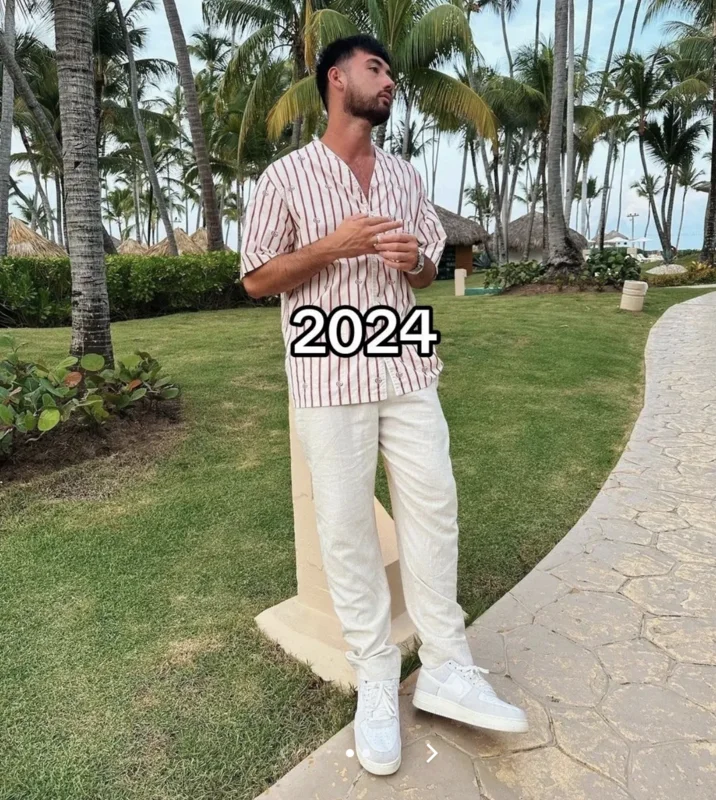 Noah Boat N Em — Adult Noah in striped shirt and cream pants standing on a tropical resort walkway in 2024.