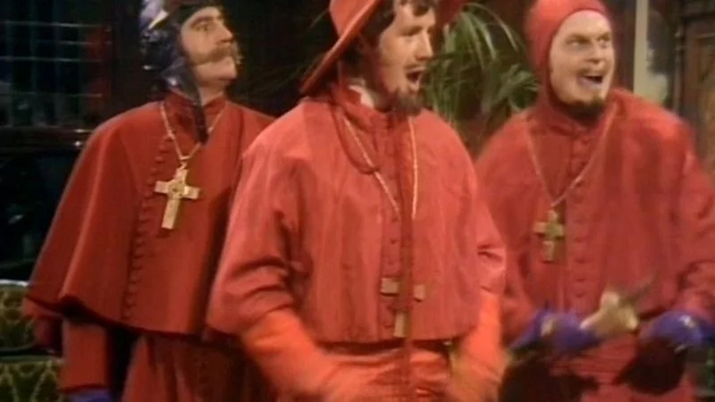 Nobody Expects the Spanish Inquisition — Original Monty Python scene showing three Spanish Inquisition characters in red robes in dark interior.