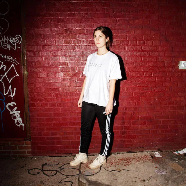 Young man in normcore outfit — light shirt, jeans, and dad sneakers — sitting on a white minivan at night