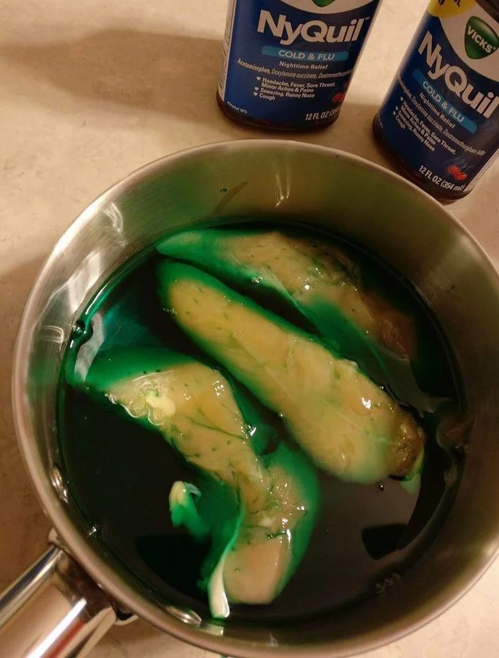 NyQuil Chicken — Two chicken tenders cooking in green NyQuil liquid in a saucepan next to two NyQuil bottles
