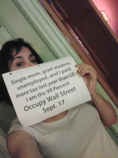 We Are The 99 Percent — Woman holds a sign reading she paid more tax than GE and that she is the 99 percent.