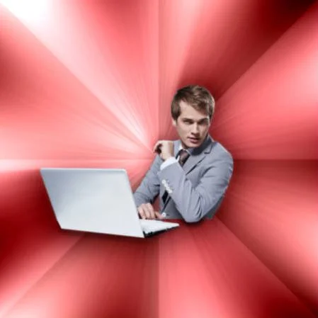 Overly Suave IT Guy — Young man in gray suit at white laptop with smug sideways glance on red starburst background